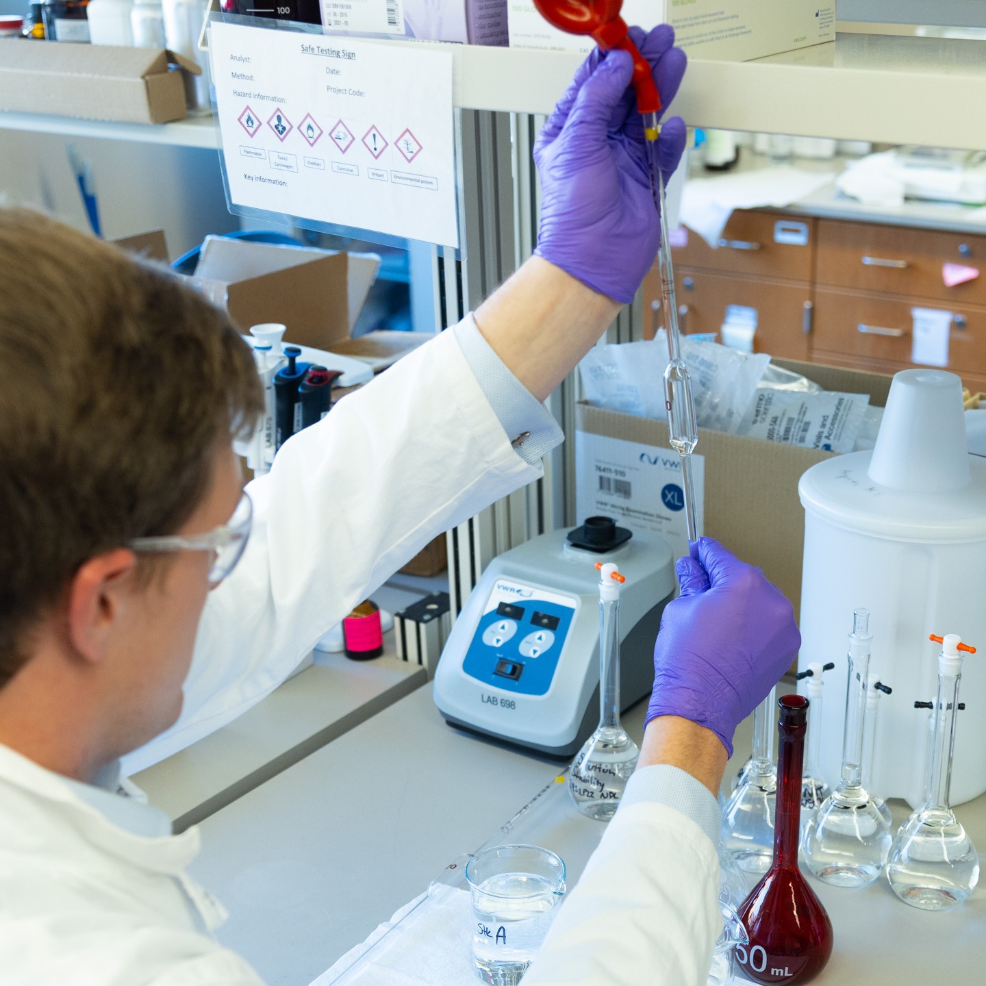 A man in a labcoat and other personal with protective equipment holds a long pipette in a lab at the Bioscience and Technology Business Incubator in Lawrence, KS.